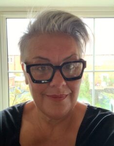 Lady with short white hair wearing glasses in front of a window