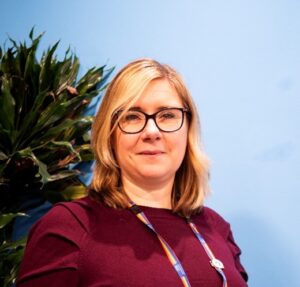 Lady smiling wearing glasses against blue backgound 